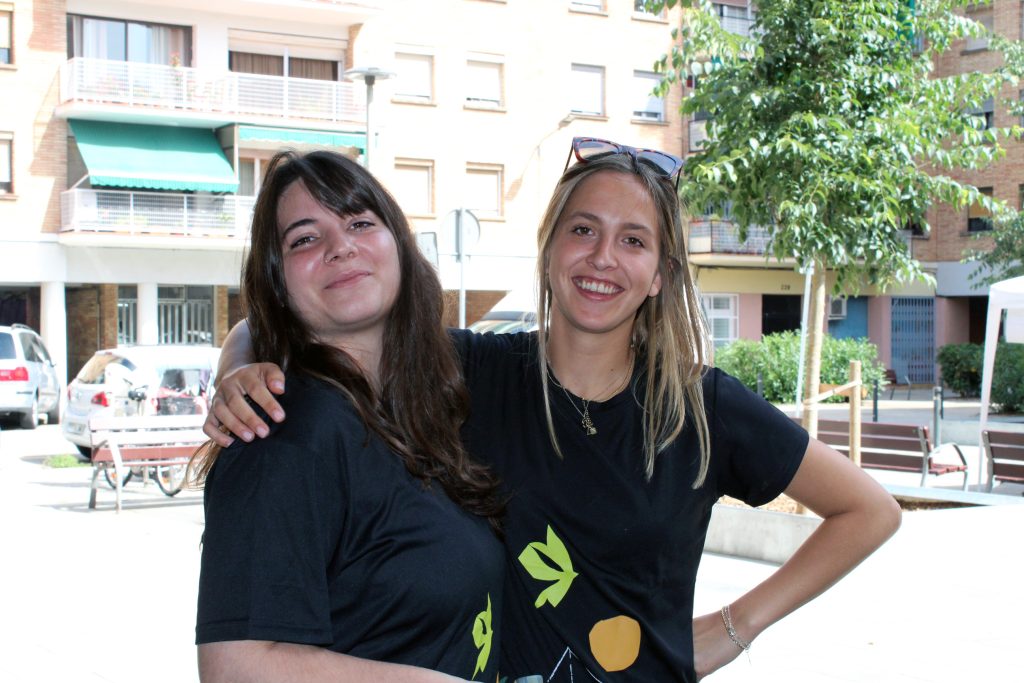 Dues assistents a la I Festa Comunitària d'Arep, mirant a càmera, amb la samarreta corporativa