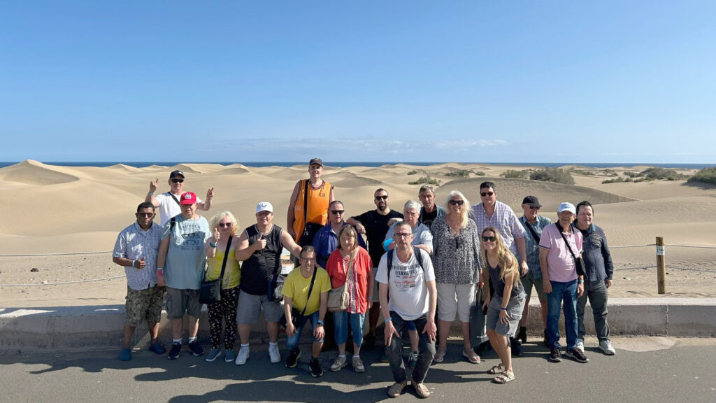 Foto de grup del Club Social, davant d'unes dunes amb el mar de fons.