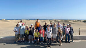 Foto de grup del Club Social, davant d'unes dunes amb el mar de fons.