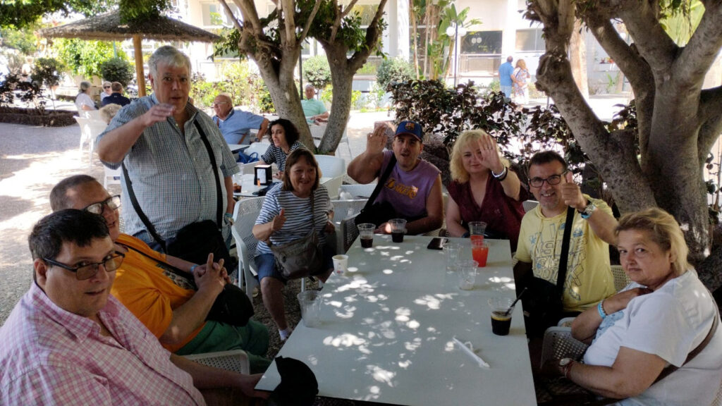 Foto de grup del club social, asseguts al voltant d'una taula a l'exterior sota l'ombra d'uns arbres.