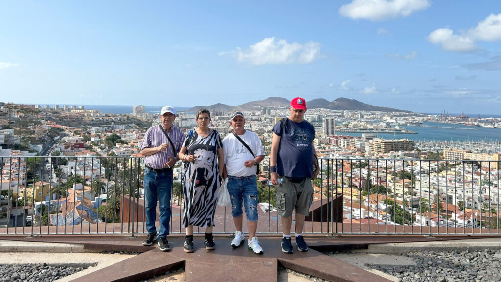 Quatre persones al davant d'una barana d'un mirador, amb una ciutat i unes muntanyes al fons.