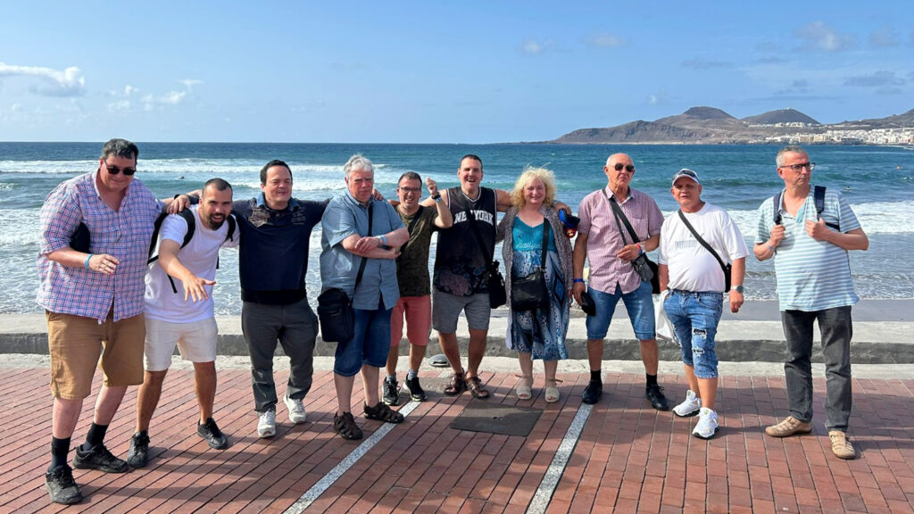 Foto de grup del Club Social, en un passeig marítim al davant d'una platja amb onades.