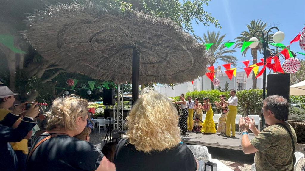 La terrassa d'un hotel, amb persones assegudes d'esquena sota un para-sol, mirant un espectacle de balls tradicionals.