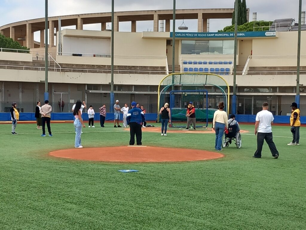 Diverses persones reunides al voltant d'un camp de beisbol, gaudint de l'ambient i l'activitat esportiva.