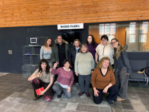 Foto de grup de 10 dones en dues files, les del davant ajupides, davant d'un estudi de ràdio amb el logotip de Ràdio Fabra.