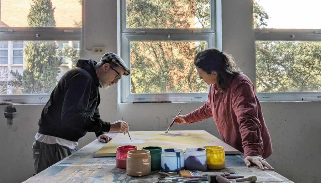 Dues persones treballant en una pintura a sobre d'una taula en un taller creatiu.