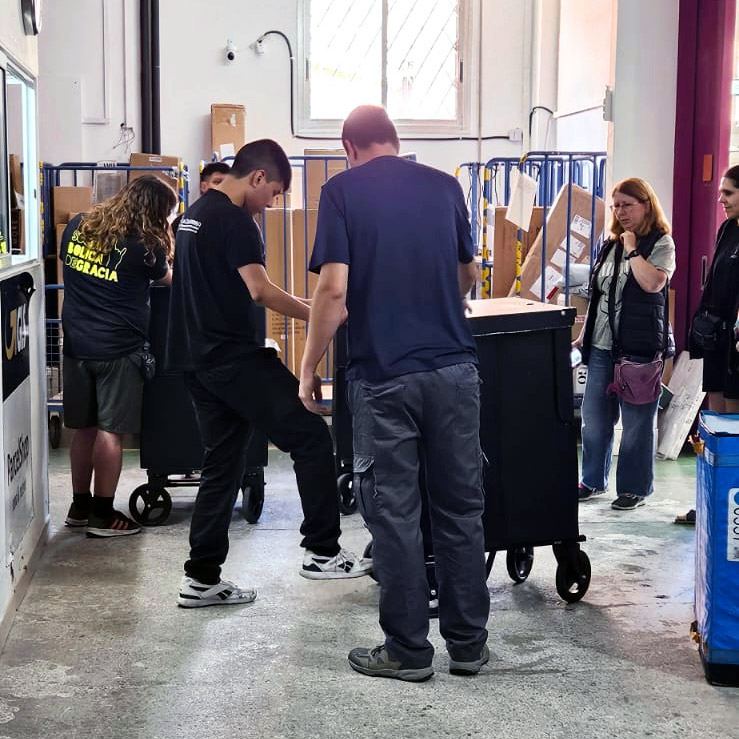 Diverses persones amb roba de feina probant uns carros de repartiment en un moll de càrrega.