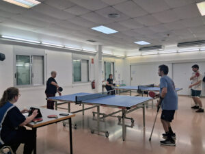 Un grup de persones jugant a ping-pong en diferents taules disposades en una sala gran.