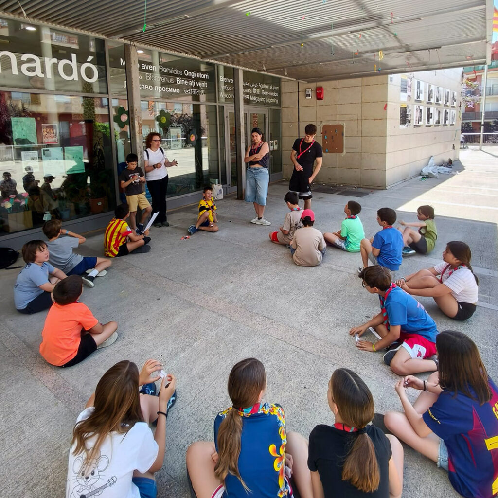 Un grup d'adolescents asseguts en rotllana escoltant l'explicació d'una persona adulta.