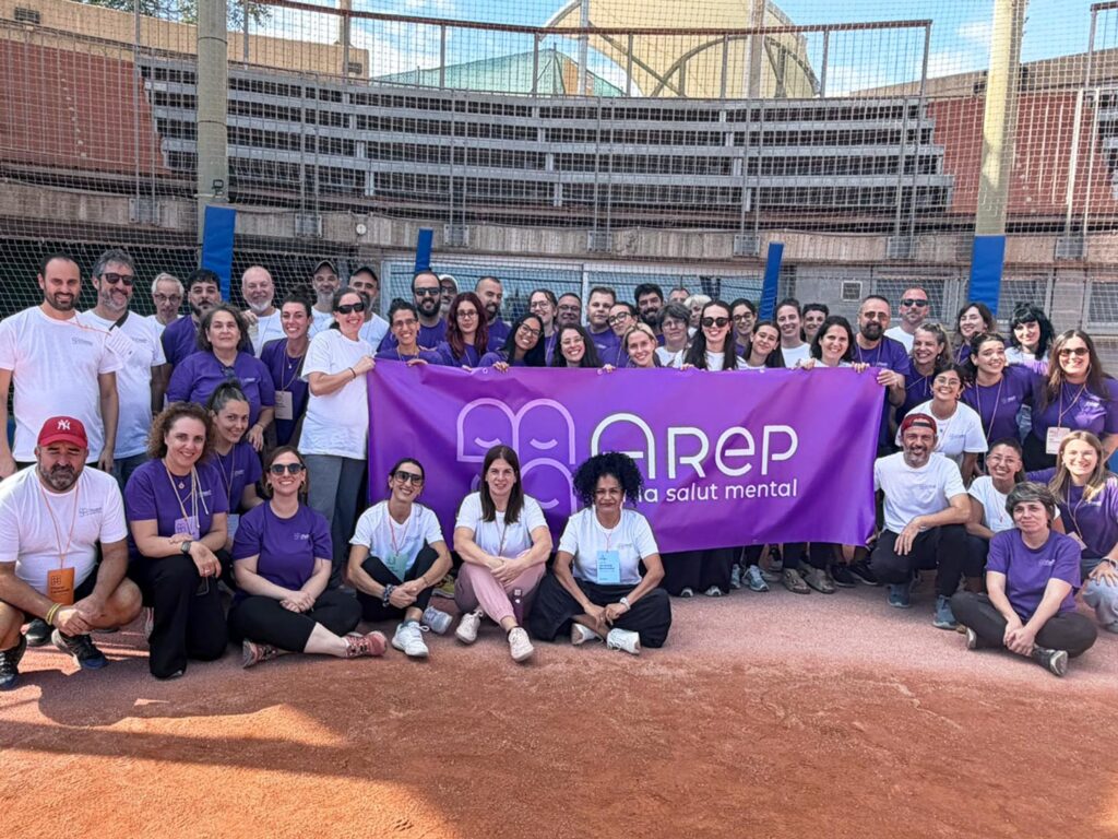 Foto grupal d'unes 60 persones en un camp de beisbol, subjectant una lona amb el logo d'Arep