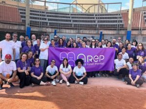 Foto grupal d'unes 60 persones en un camp de beisbol, subjectant una lona amb el logo d'Arep