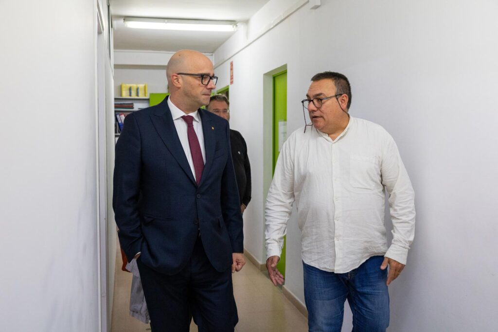 Dos homes, un d'ells amb vestit i corbata, es desplacen per un passadís durant una reunió professional.