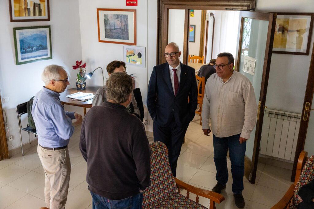 Grup de persones dempeus en una sala amb fotografies decorant les parets.