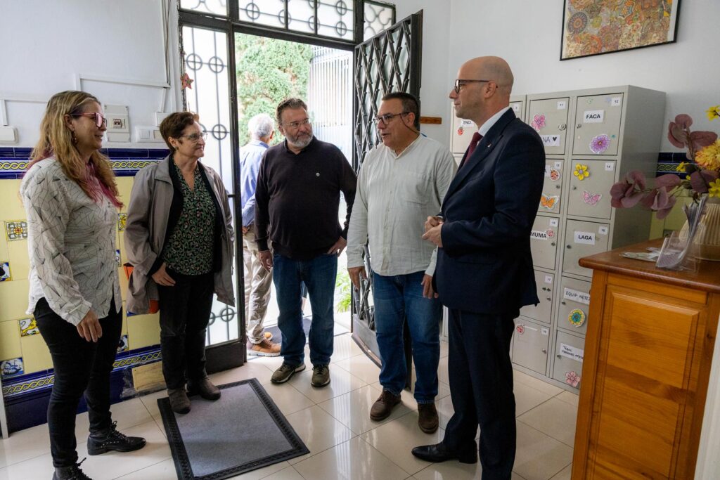 Grup de persones dempeus davant d'una porta, conversant i somrient entre si.